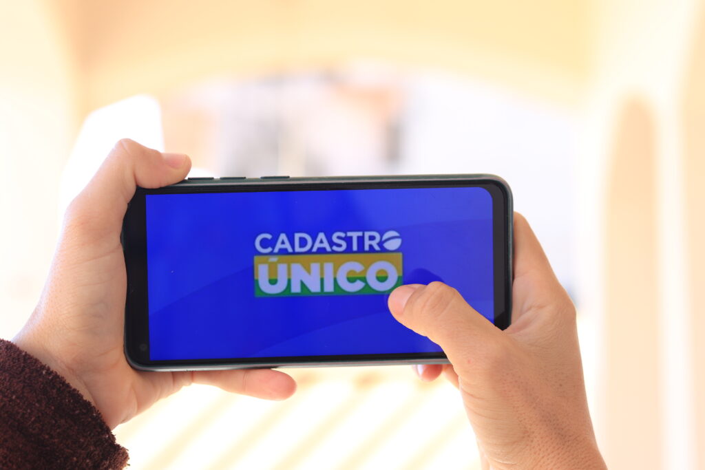Pessoa segurando celular na horizontal no app CadÚnico.